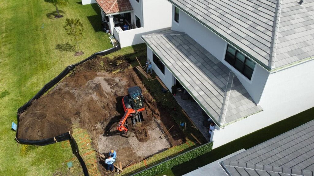 Common Mistakes to Avoid When Hiring a Pool Builder 3 Aerial view of a backyard pool excavation site, with a mini-excavator digging a large hole and workers nearby.