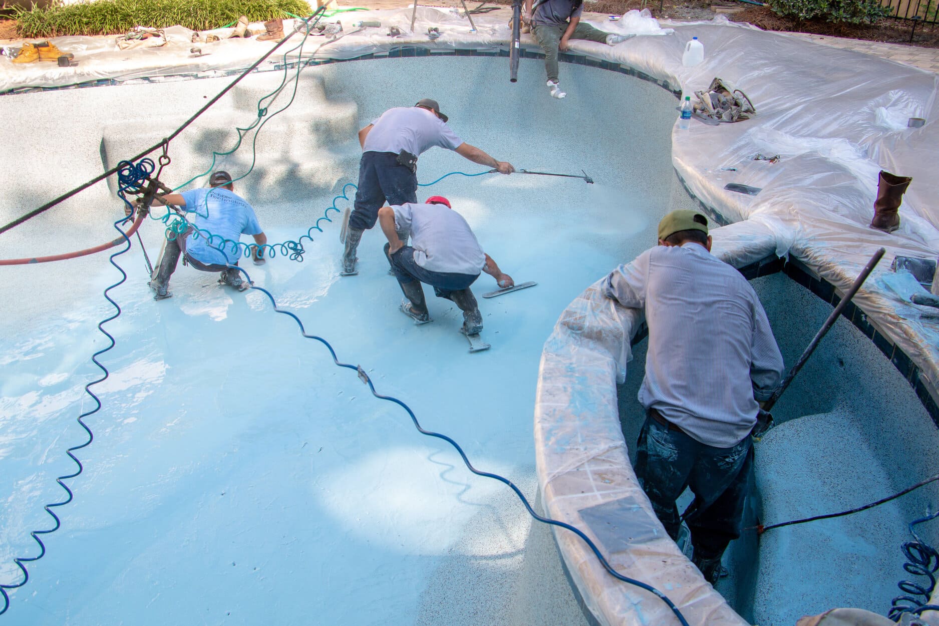 Construction workers applying gunite to the walls of a newly dug swimming pool.