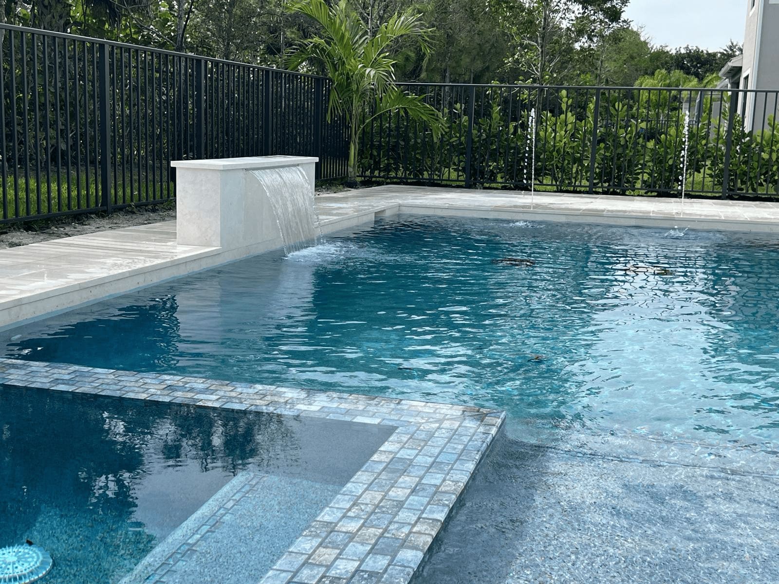 A new in-ground pool with a raised jacuzzi, decorative waterfall, and white patio pavers.