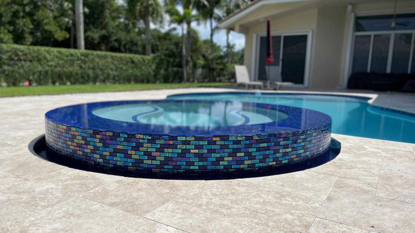 A newly installed round jacuzzi with a blue iridescent mosaic tile exterior and a stone patio.