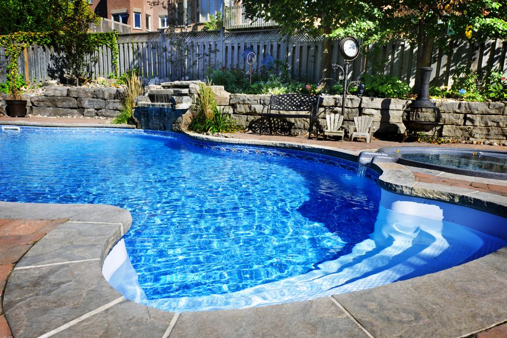 A luxury in-ground pool with a rock waterfall, hot tub, and stone retaining wall.