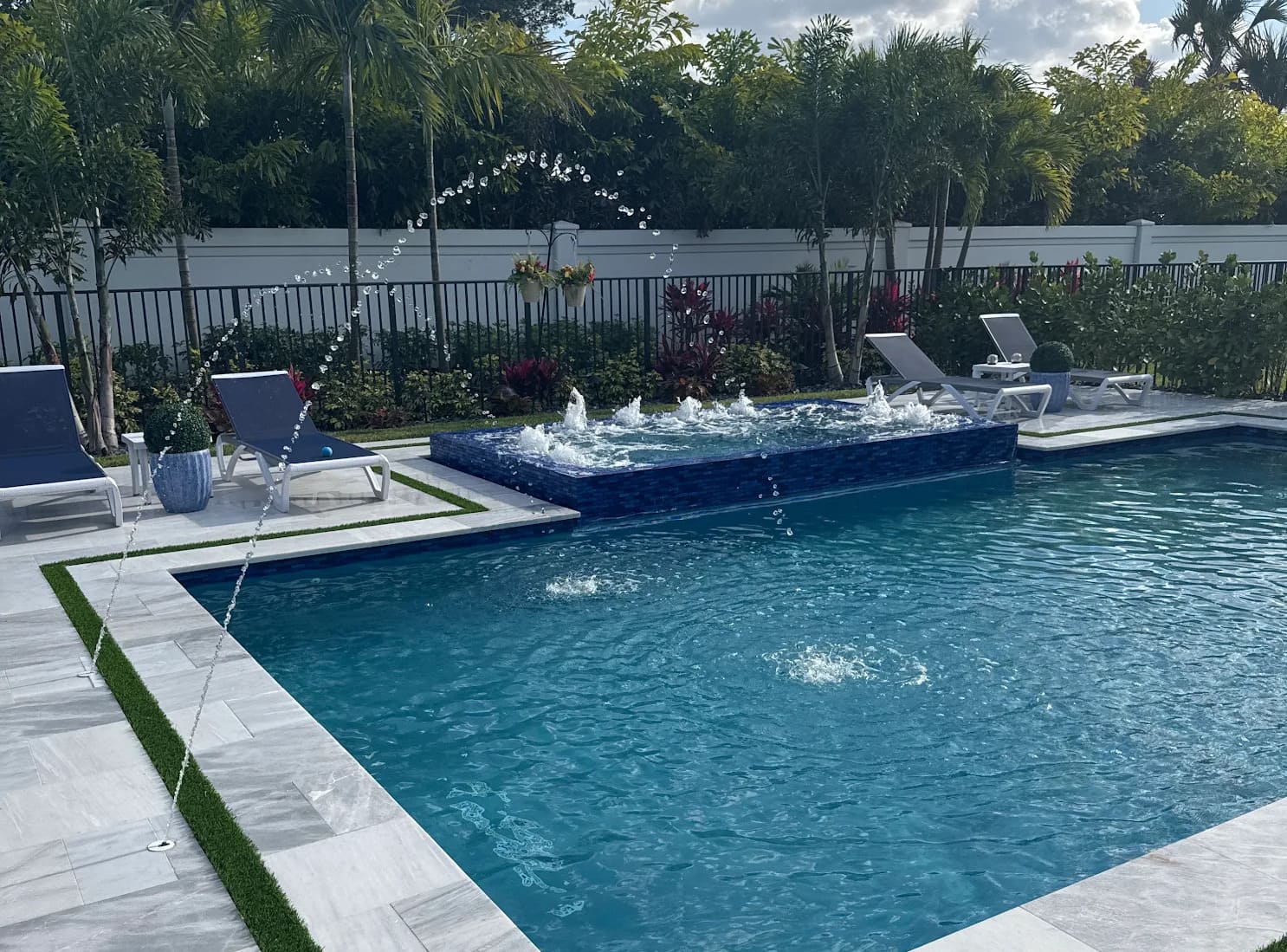 A modern in-ground pool with fountains, a raised jacuzzi, and a white marble patio.