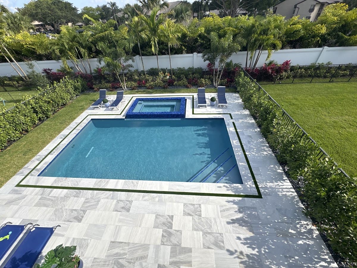 An aerial or high-angle view of a rectangular backyard pool with an elevated hot tub. The hot tub features a striking blue mosaic tile exterior.