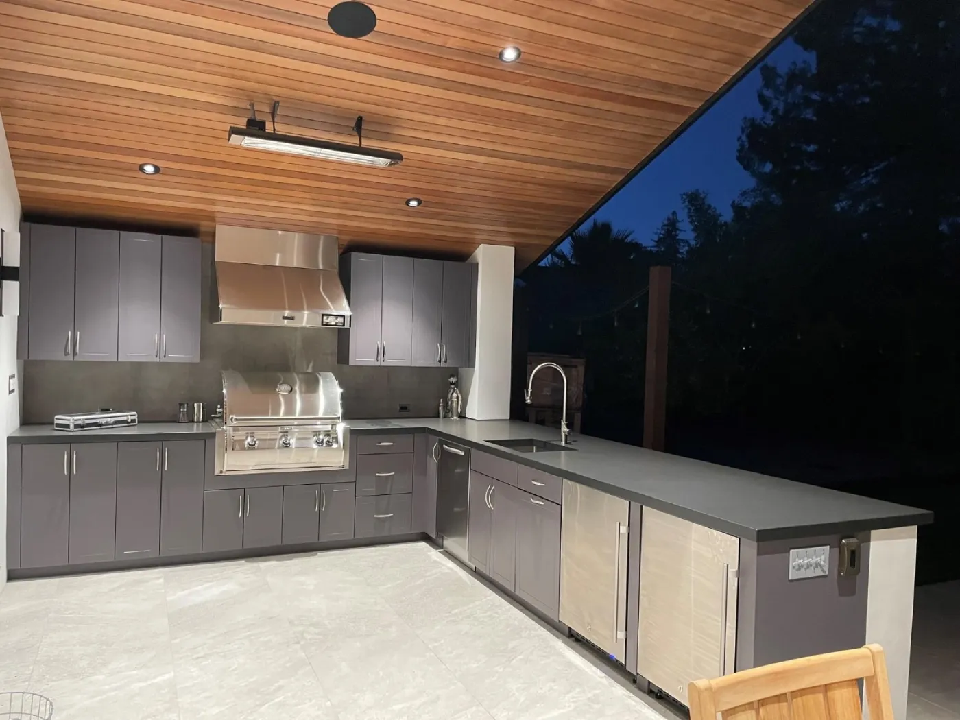 An outdoor kitchen area with a dark blue cabinet base, a white granite countertop, a built-in kegerator, and a grill. It's located under a screened enclosure next to a pool.