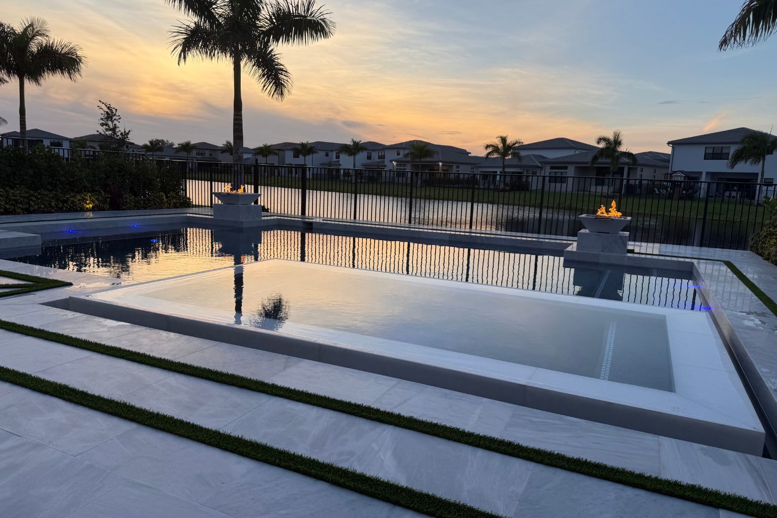 Stunning custom pool with clean lines, tranquil water features, and a modern design, featuring a fire fountain, reflecting the serene backyard ambiance at sunset