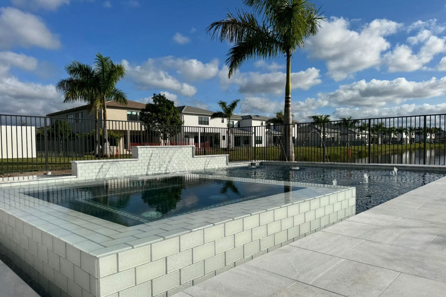 user-inserted Luxury Florida backyard pool with elevated spa, modern white tile decking, and palm trees, ideal for outdoor entertaining and high-end residential design.