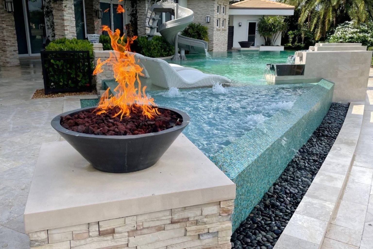 Luxury modern Florida pool with integrated fire feature, infinity edge spa, and surrounding patio seating showcasing premium outdoor living design and heated pool benefits.