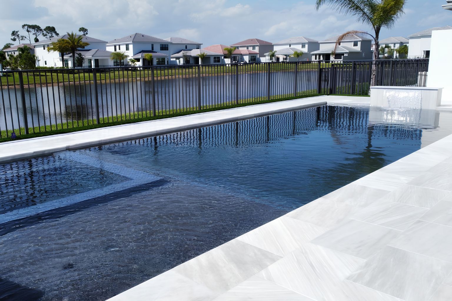 user-inserted Modern geometric luxury pool in Boca Raton, Florida with infinity edge, clean white tile decking, spa area, and backyard view of lake and palm trees