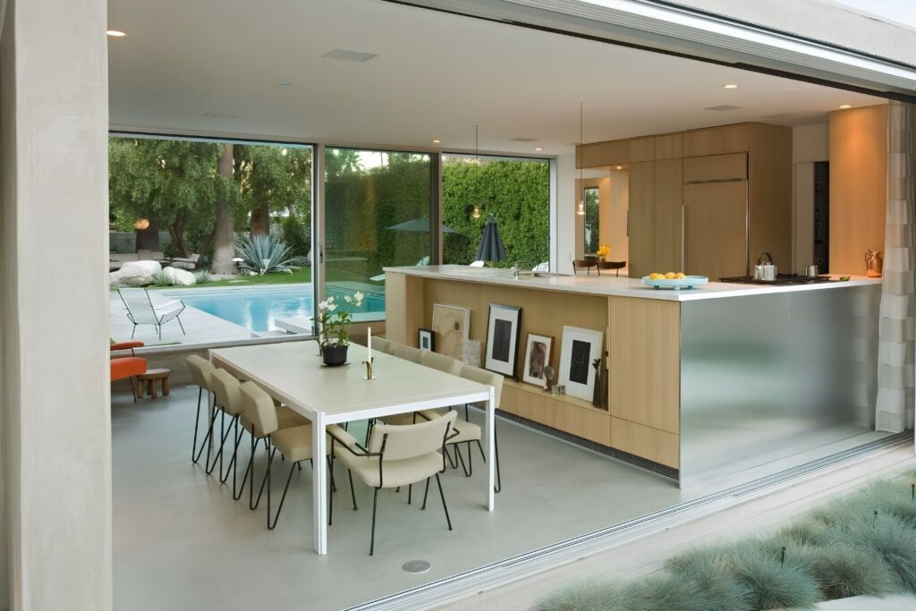 Modern open-concept kitchen and dining area with sleek cabinetry, minimalist furniture, and floor-to-ceiling glass doors overlooking a luxury backyard pool and patio, ideal for indoor-outdoor living inspiration.