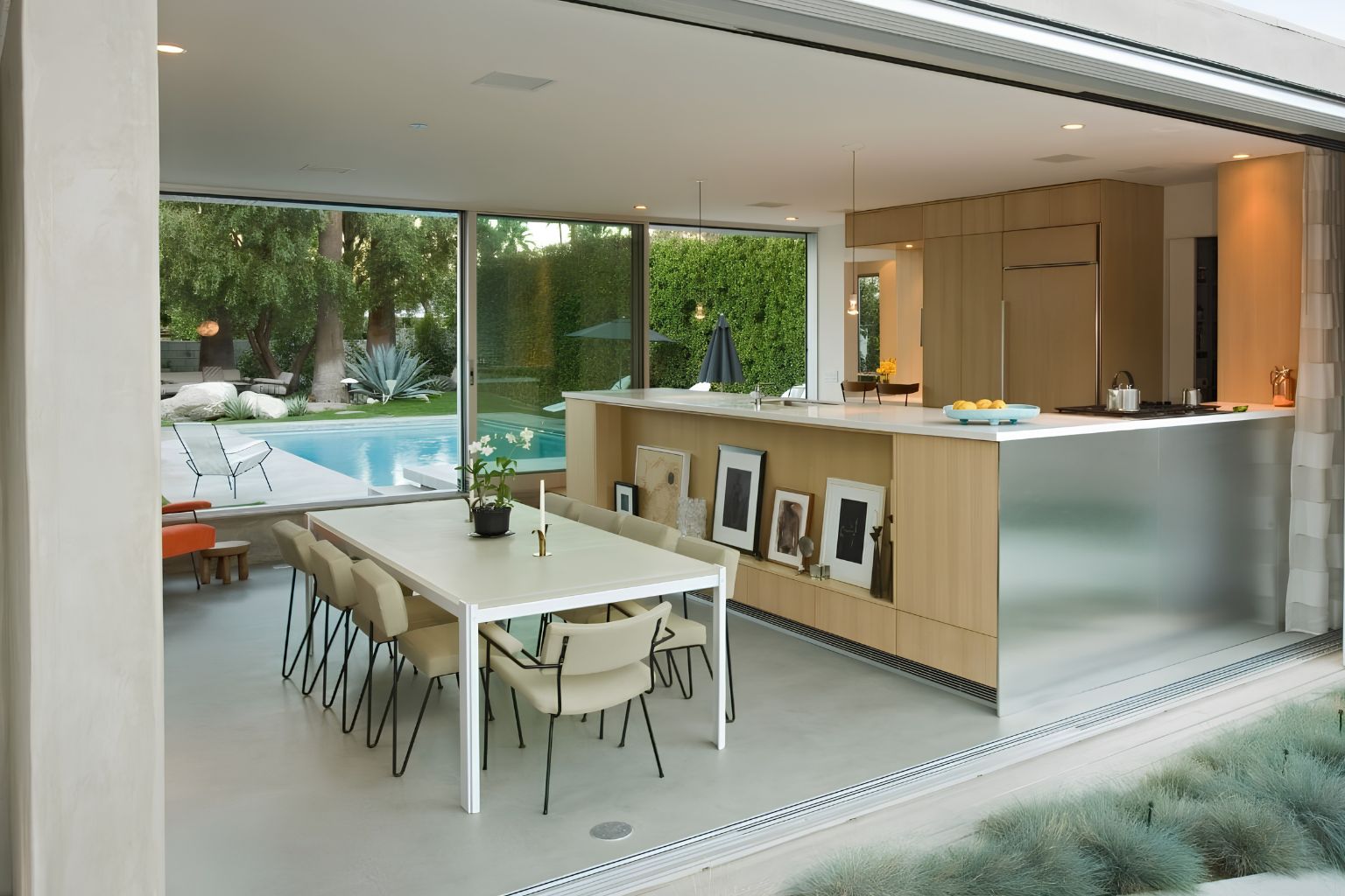 Modern open-concept kitchen and dining area with sleek cabinetry, minimalist furniture, and floor-to-ceiling glass doors overlooking a luxury backyard pool and patio, ideal for indoor-outdoor living inspiration.