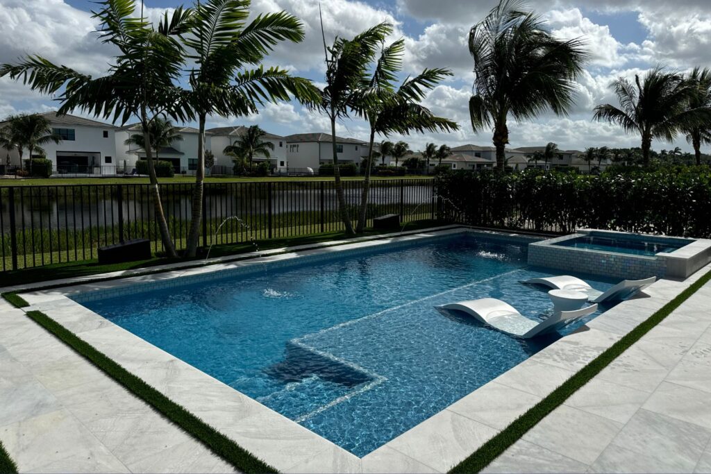 Modern Florida backyard pool design with integrated spa, white tiled decking, lounge chairs in shallow sun shelf, and landscaped greenery, showcasing luxury outdoor living.