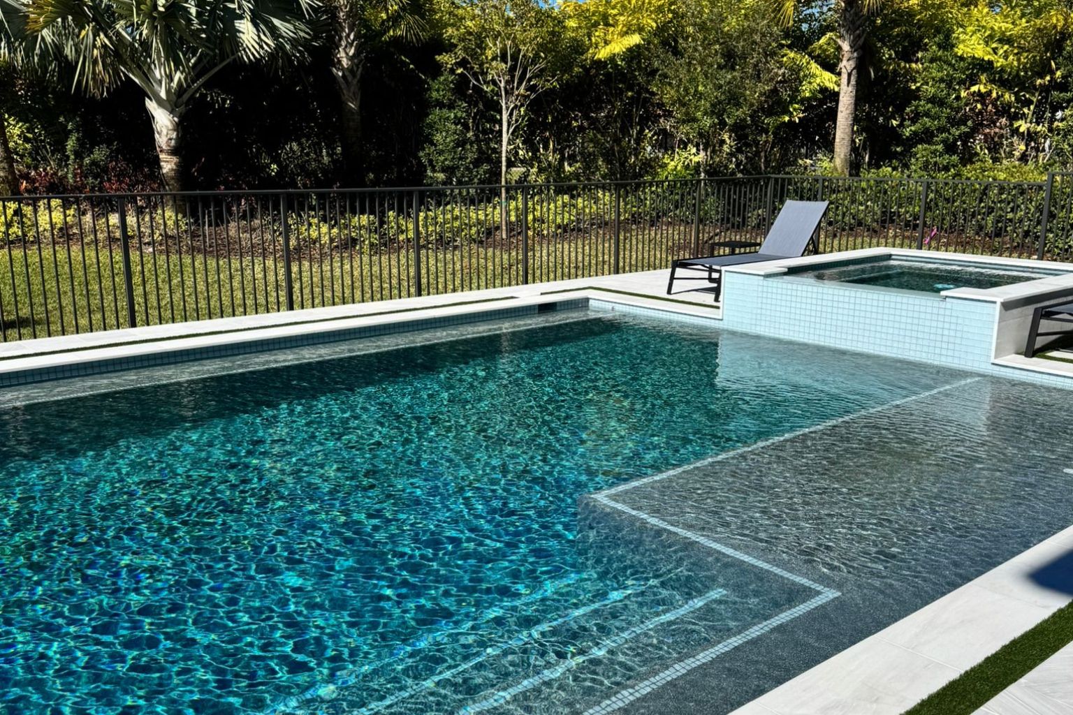 Luxury backyard pool in Florida with spa, sun shelf, and modern design, showcasing clear blue water, white tile deck, and private tropical landscaping, perfect for leisure and entertainment.