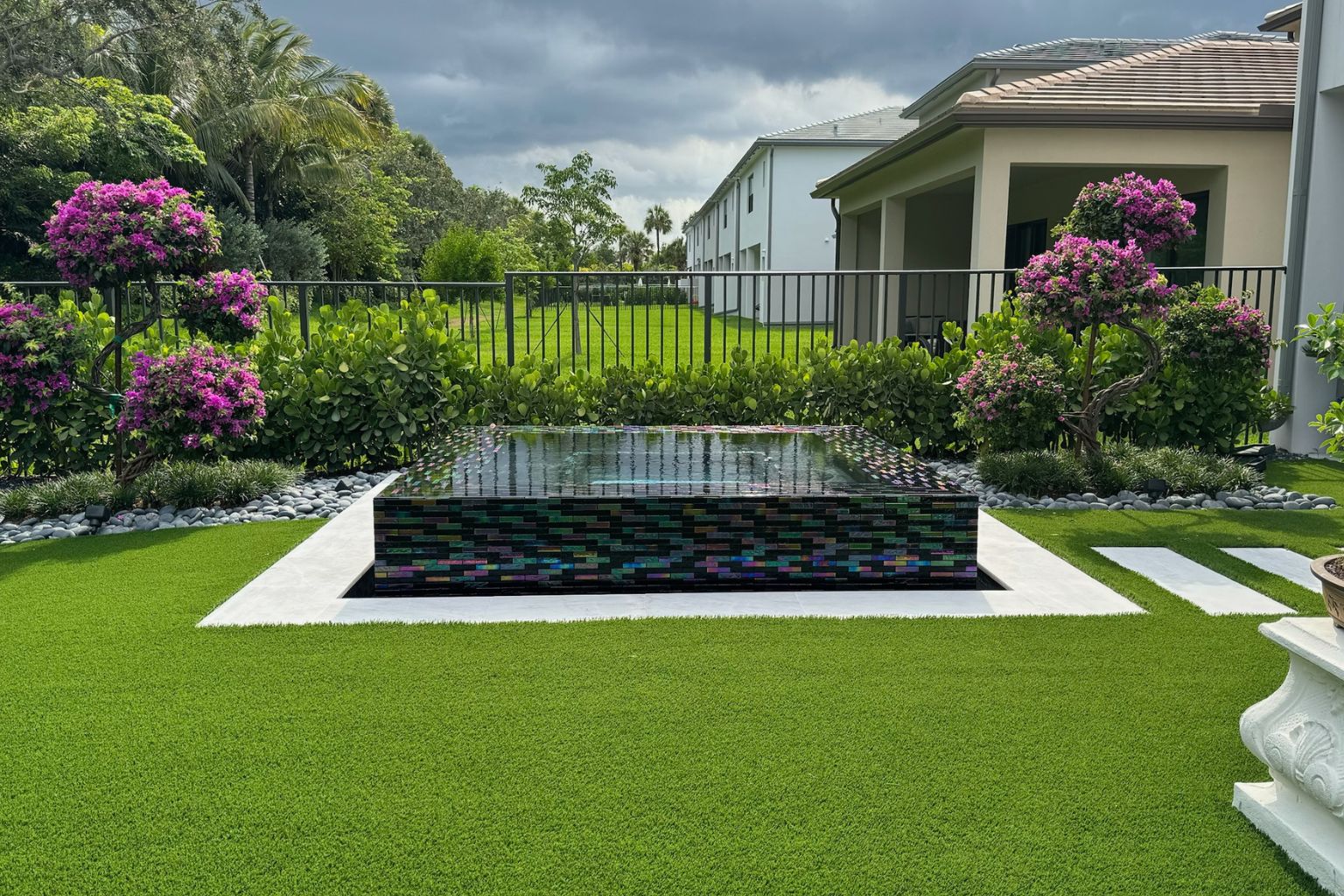 user-inserted Artificial turf backyard with pool spa, paver walkway, tropical landscaping, and low-maintenance synthetic grass.