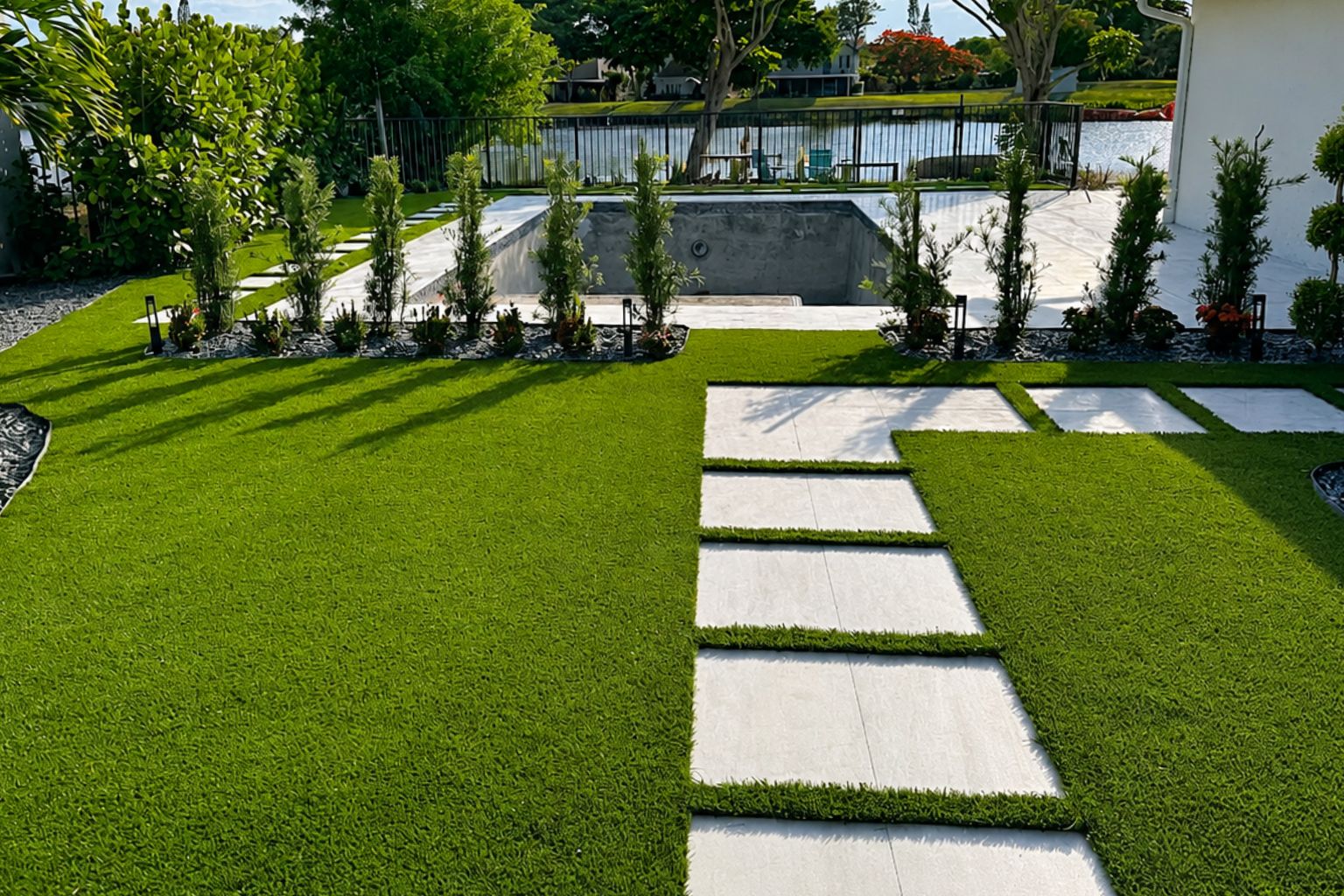 Backyard artificial turf installation with stepping stone pathway around a custom pool, landscaped beds, and modern outdoor living space.