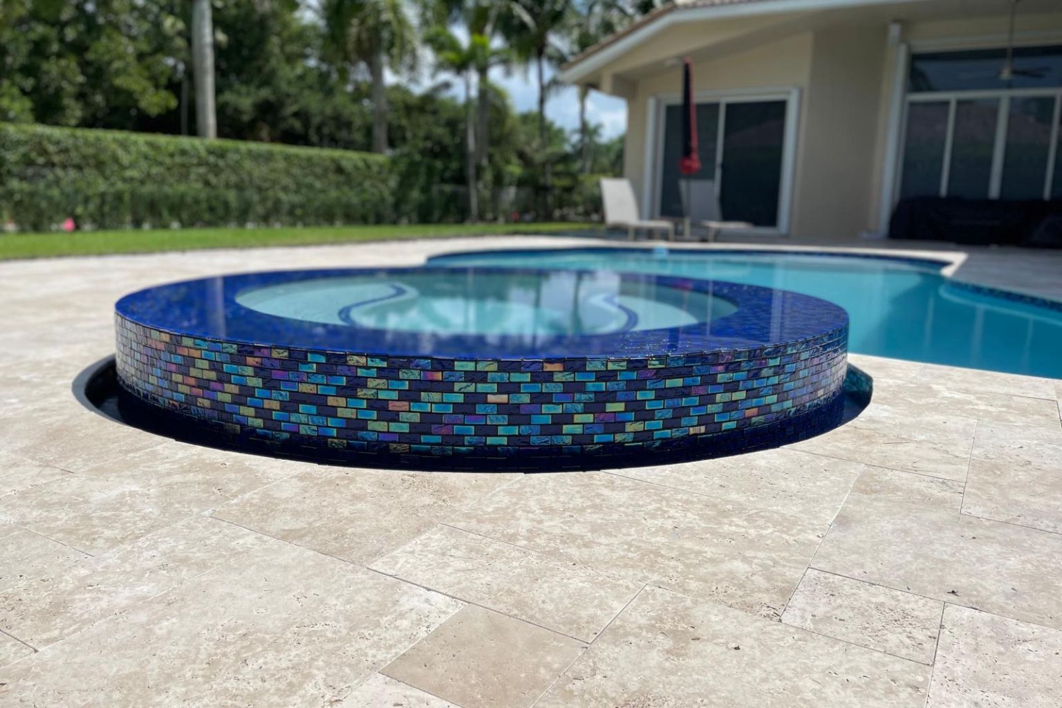user-inserted Natural marble pool deck with raised mosaic-tile spa, luxury backyard pool, and light stone pavers.