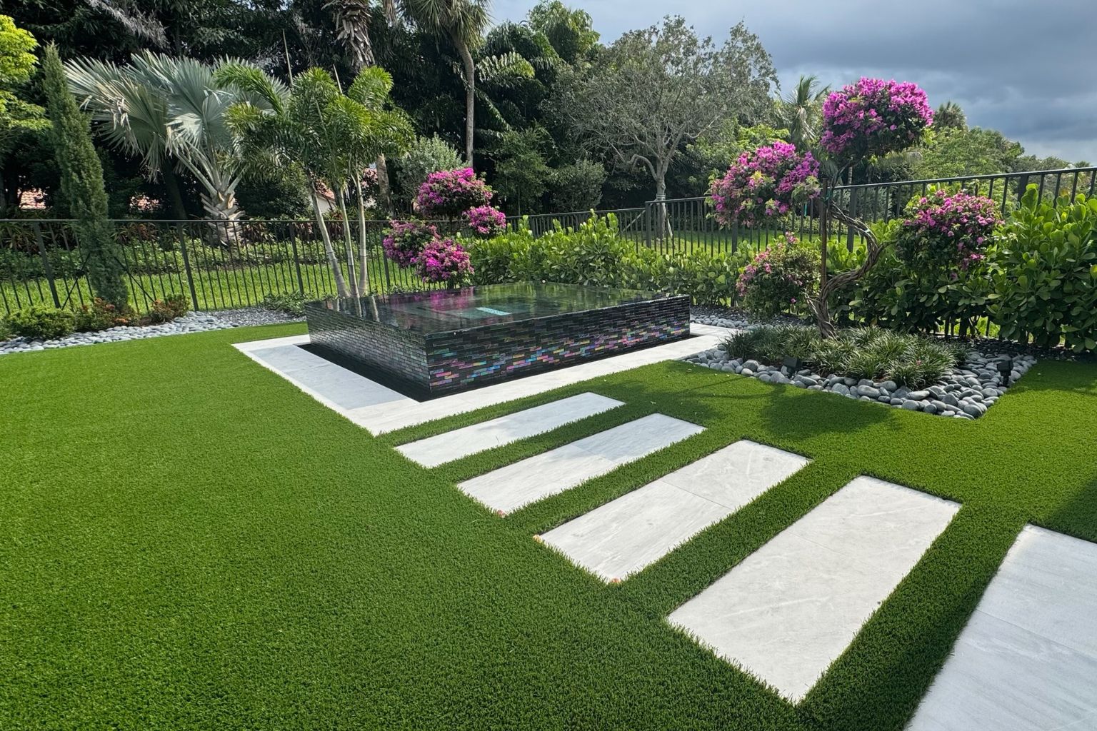 user-inserted Pet-friendly artificial turf around a pool spa with stepping stones, tropical landscaping, and low-maintenance backyard design.