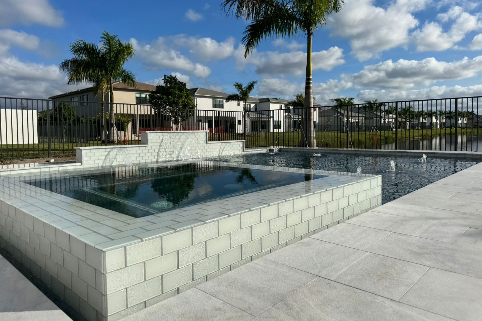 user-inserted Modern pool and raised spa with light porcelain pool deck, palm trees, waterfront view, and luxury outdoor living space.